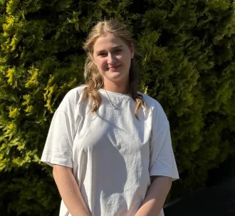 Жінка стоїть на сонці перед зеленими кущами