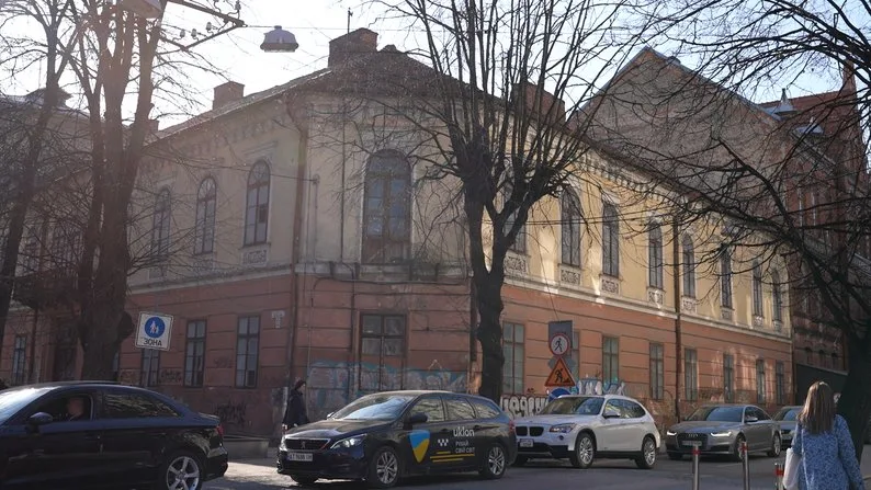 Стара будівля на вулиці з припаркованими автомобілями