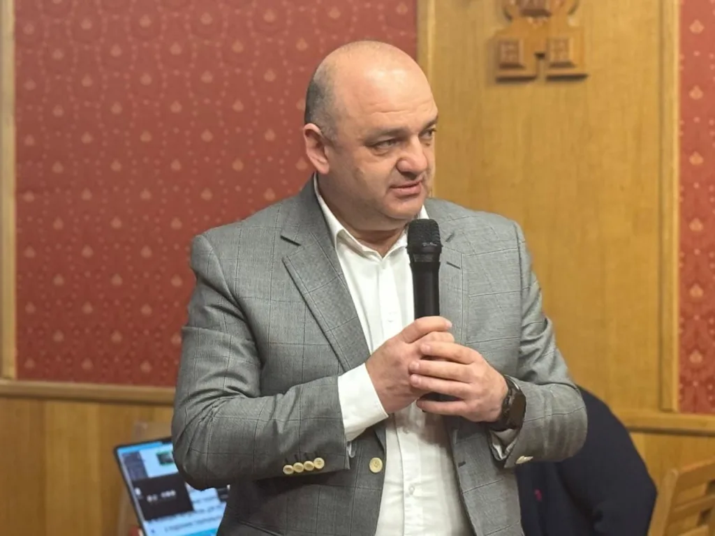 Чоловік у сірому костюмі говорить у мікрофон