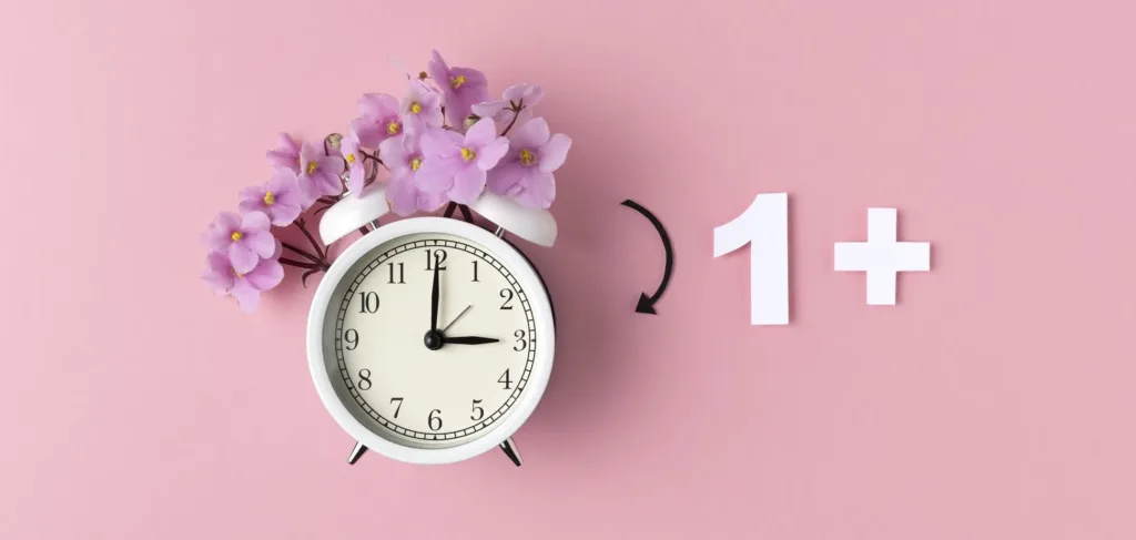 Білий будильник з фіолетовими квітами на рожевому фоні