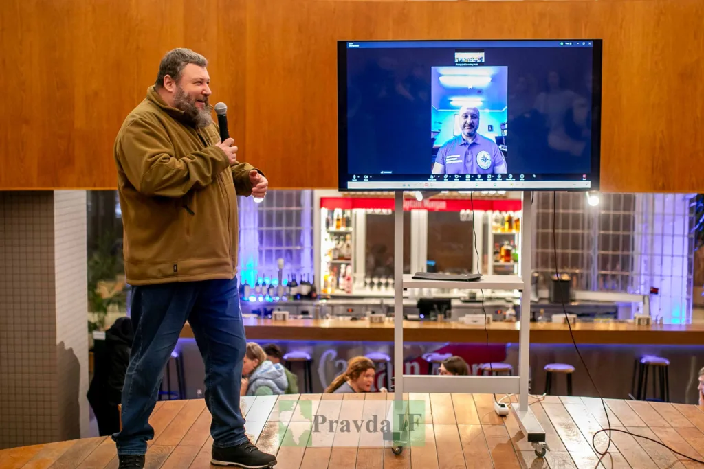 Чоловік виступає з мікрофоном перед екраном із відеодзвінком