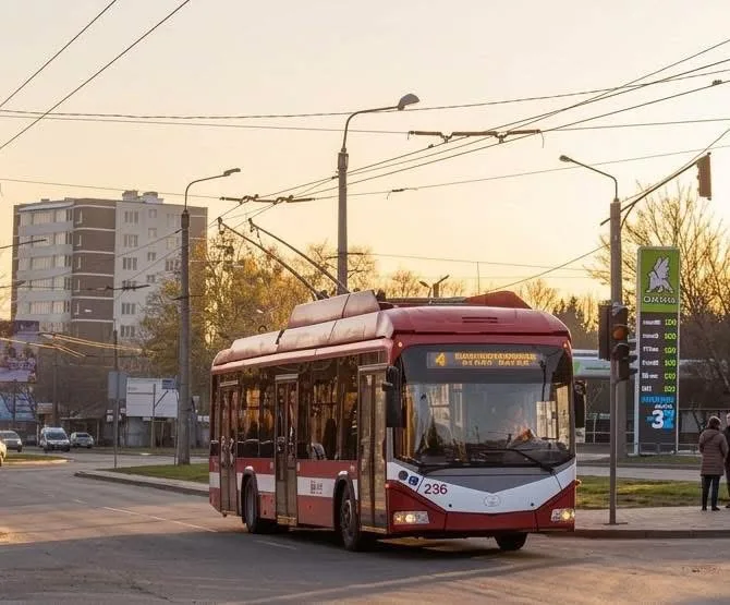 Червоний тролейбус їде міською вулицею на заході сонця