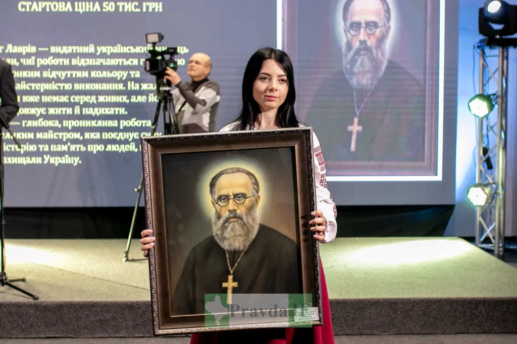 Жінка тримає портрет священика на сцені