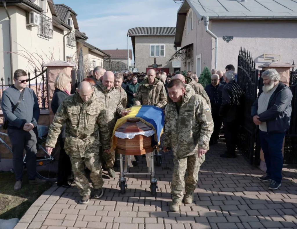 Військові несуть труну, накриту українським прапором