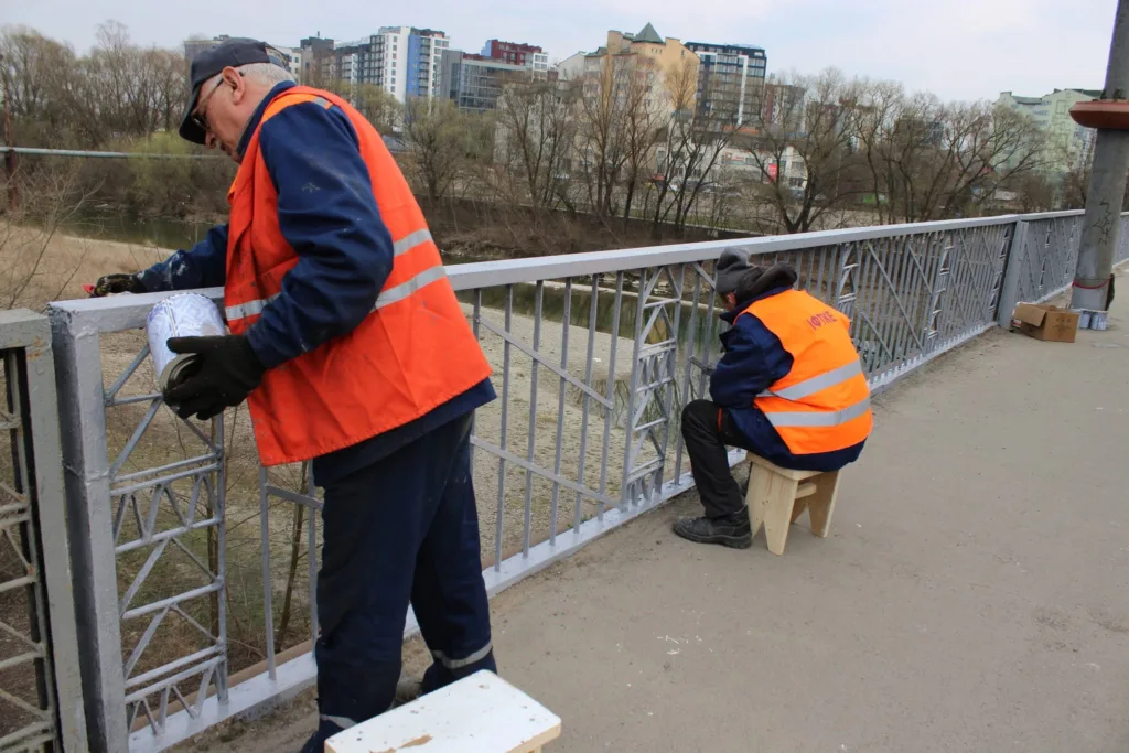 Робітники фарбують металеву огорожу мосту