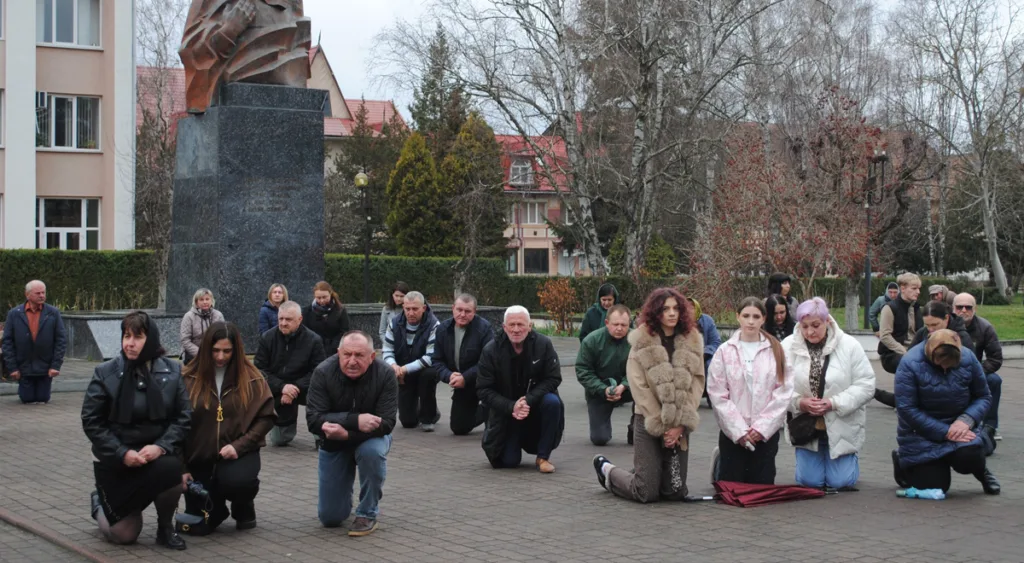 Люди на колінах біля пам'ятника у місті