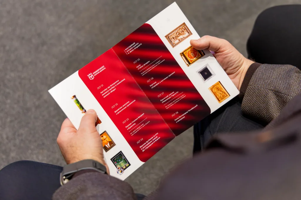 Людина тримає буклет аукціону з червоним дизайном