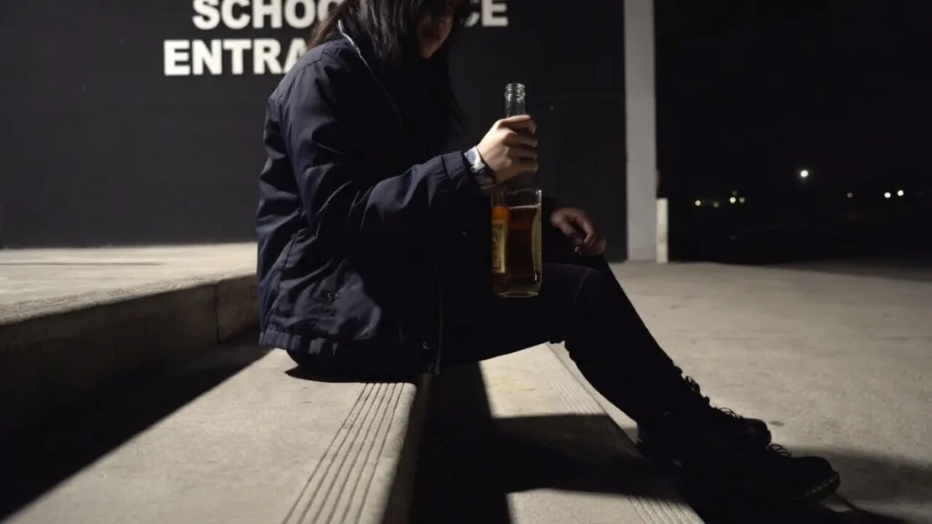 Підліток сидить біля школи з пляшкою алкоголю