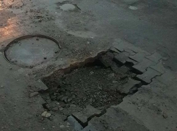 Велика яма на асфальтованій дорозі біля люка