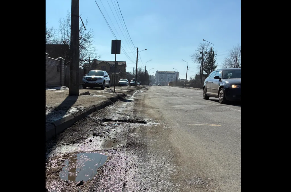 Асфальтована вулиця з вибоїнами та автівками