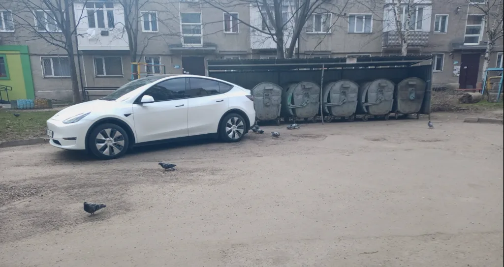 Білий автомобіль припаркований біля сміттєвих контейнерів