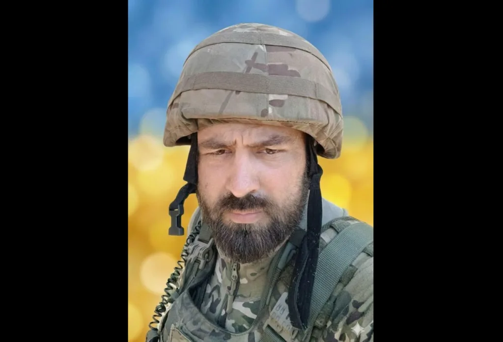 Український військовий у камуфляжі на фоні прапора