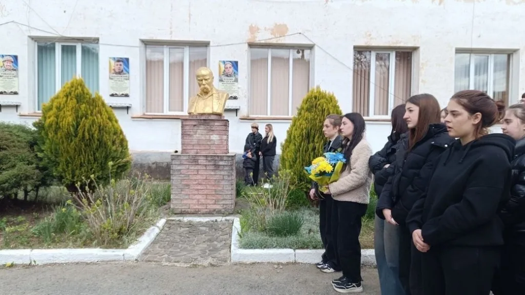 Учні вшановують памʼятник із квітами біля школи
