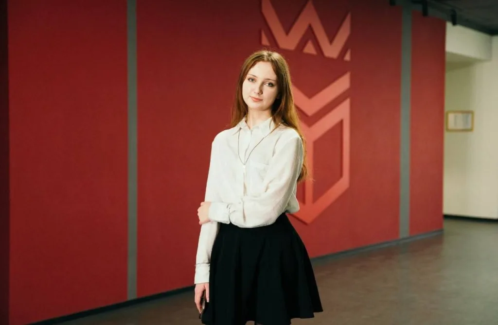 Дівчина стоїть перед червоною стіною в приміщенні