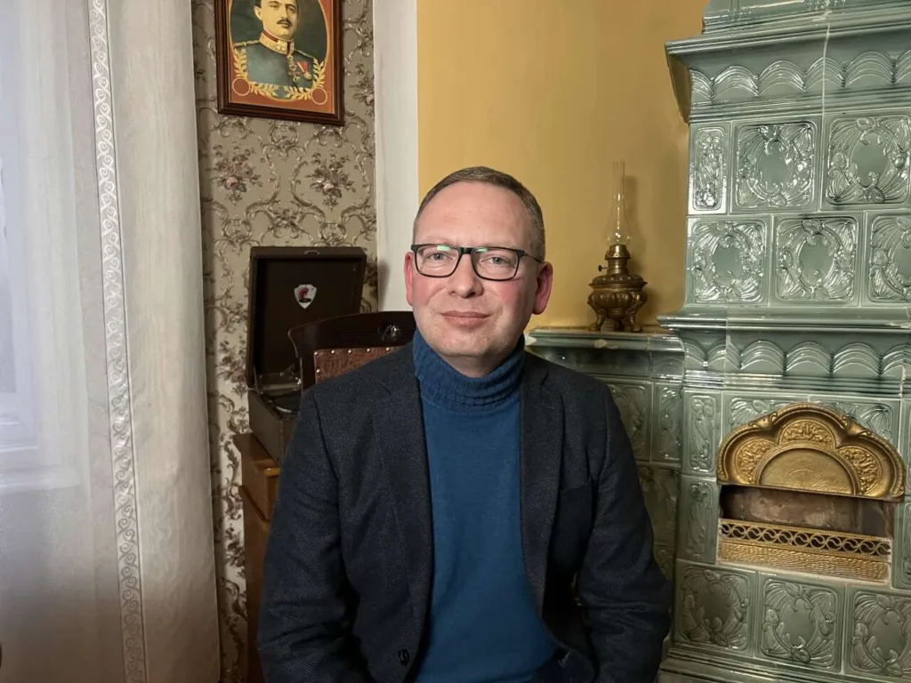 Чоловік сидить біля зеленої кахельної печі