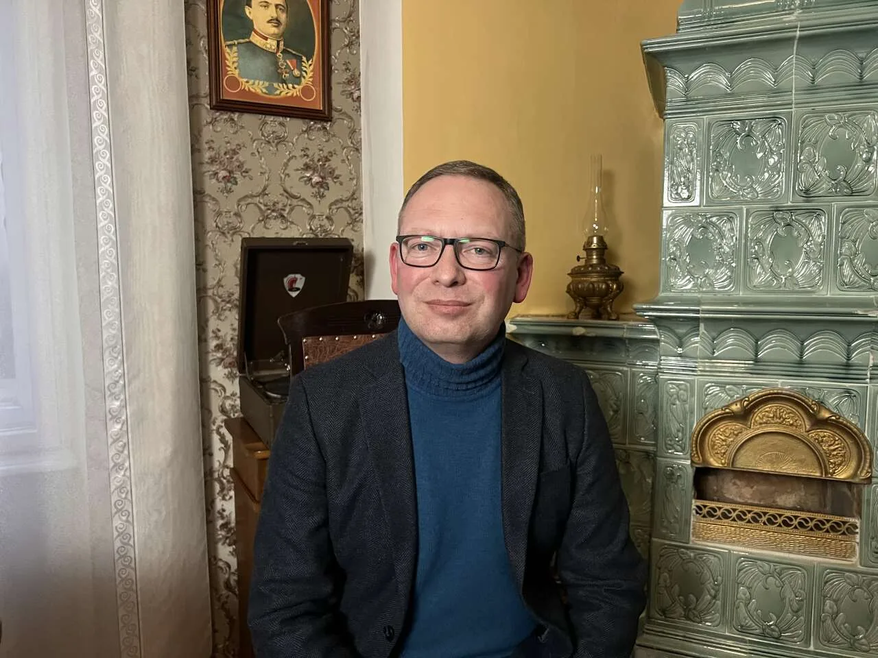 Чоловік сидить біля зеленої кахельної печі