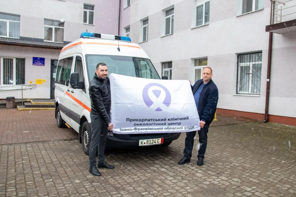 Двоє чоловіків тримають банер онкоцентру біля швидкої