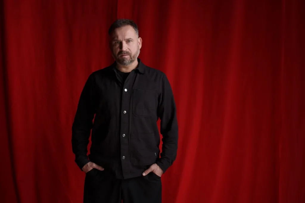 Чоловік у чорному перед червоною завісою