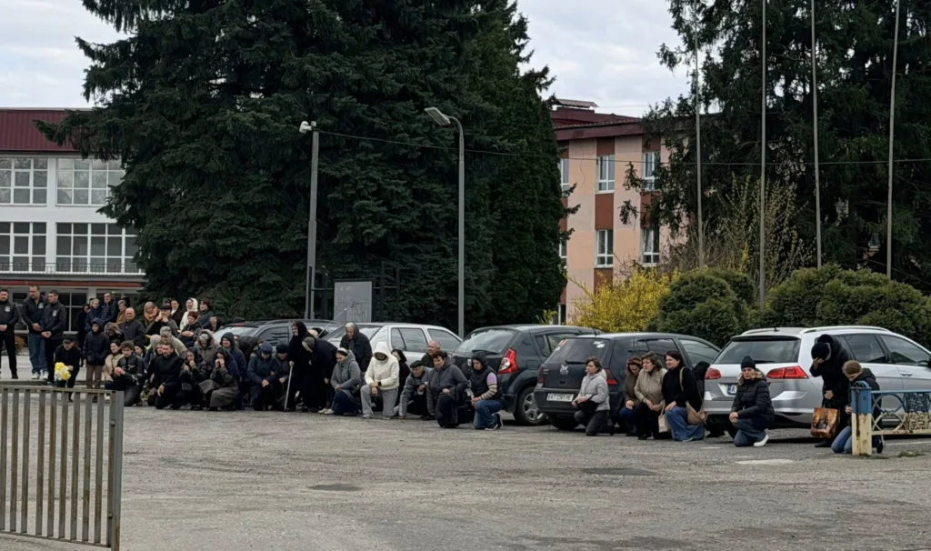 Люди на колінах біля паркувального майданчика