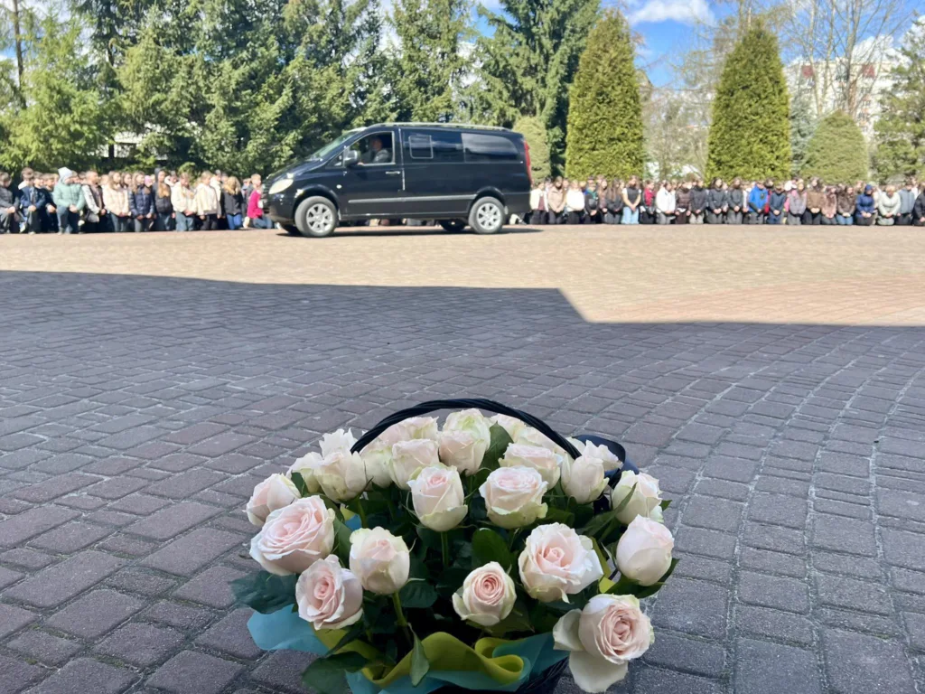 Люди на колінах проводжають чорний фургон з квітами