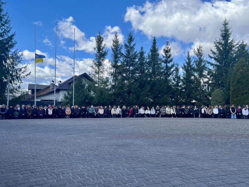 Люди стоять перед прапором України на подвір’ї.