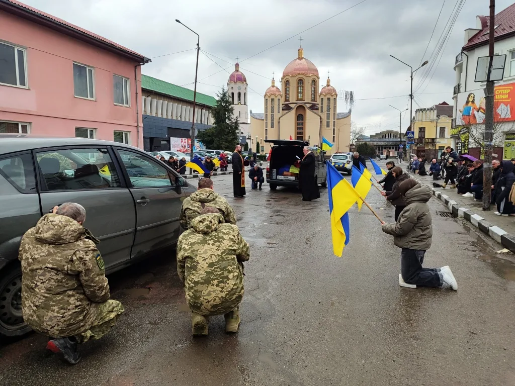 Люди з українськими прапорами на колінах біля церкви
