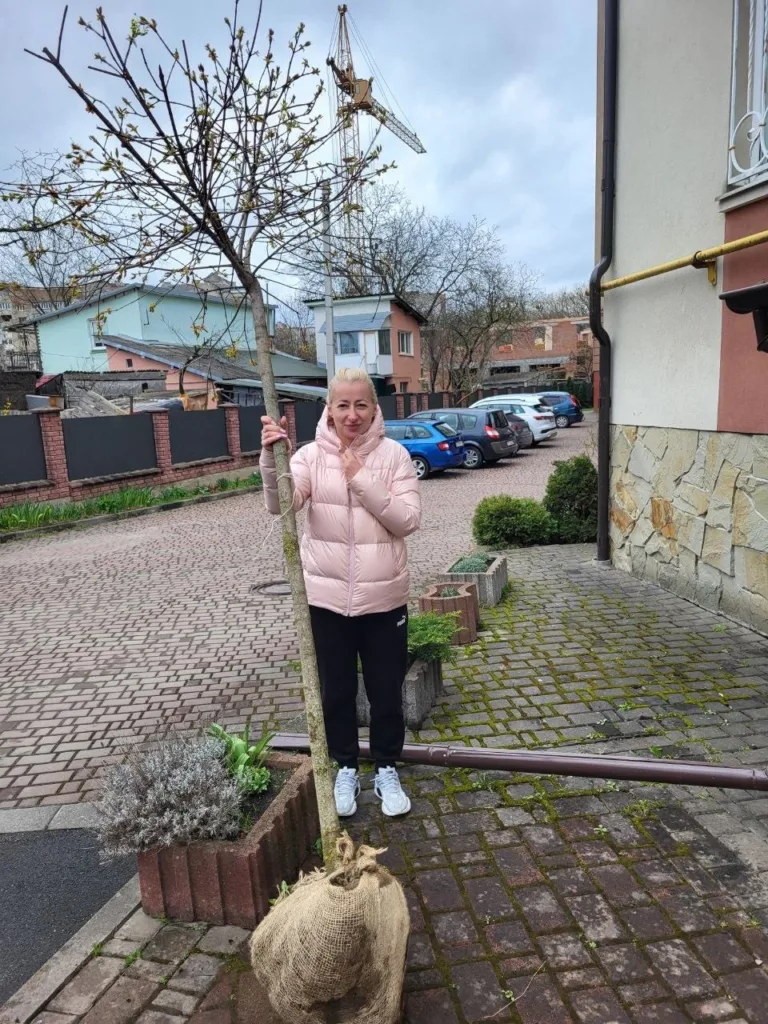 Жінка саджає дерево біля будинку