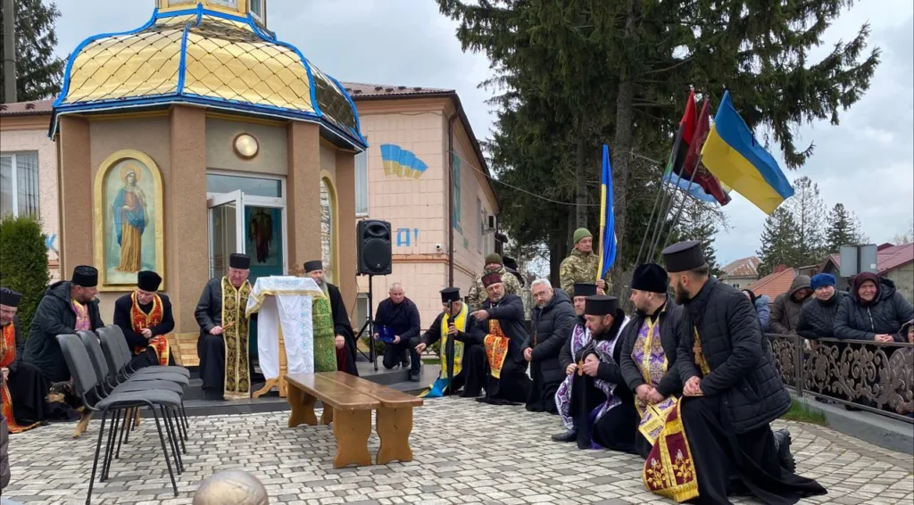 Священники моляться біля каплиці з прапорами України