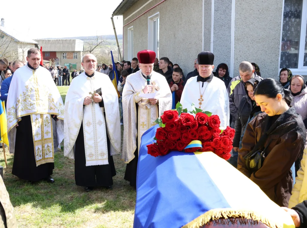 Священники та люди біля труни з прапором України
