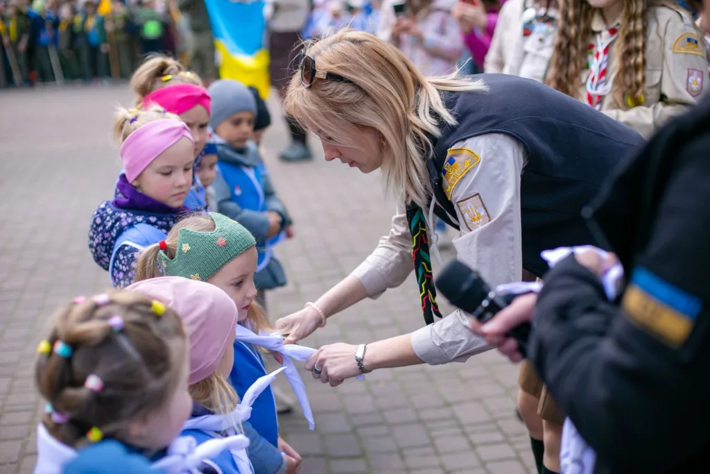 Скаутка допомагає дітям зав’язати хустки на церемонії