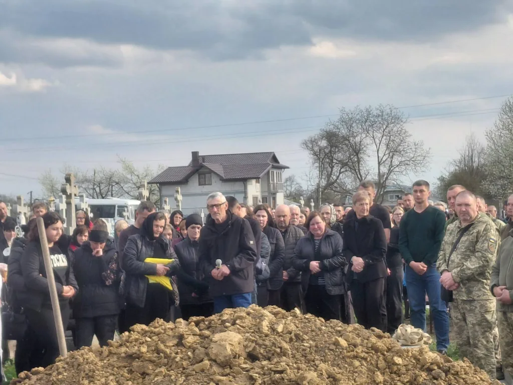 Люди на похороні на цвинтарі під похмурим небом