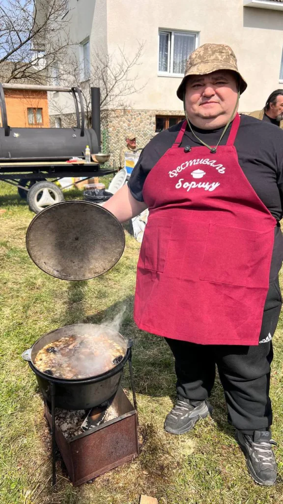 Чоловік готує борщ у казані на вогнищі