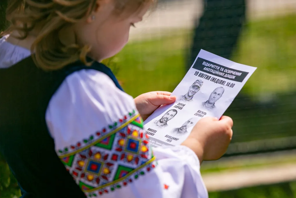 Дитина у вишиванці тримає аркуш із фото героїв