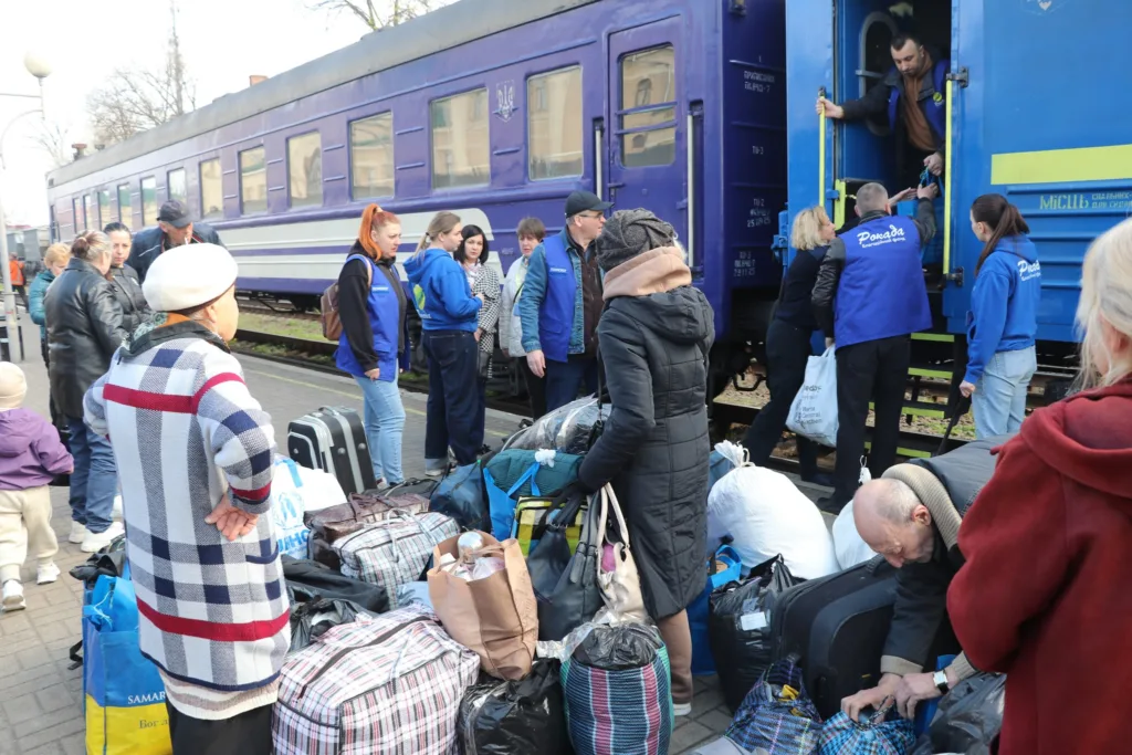 Люди з багажем біля синього потяга на вокзалі