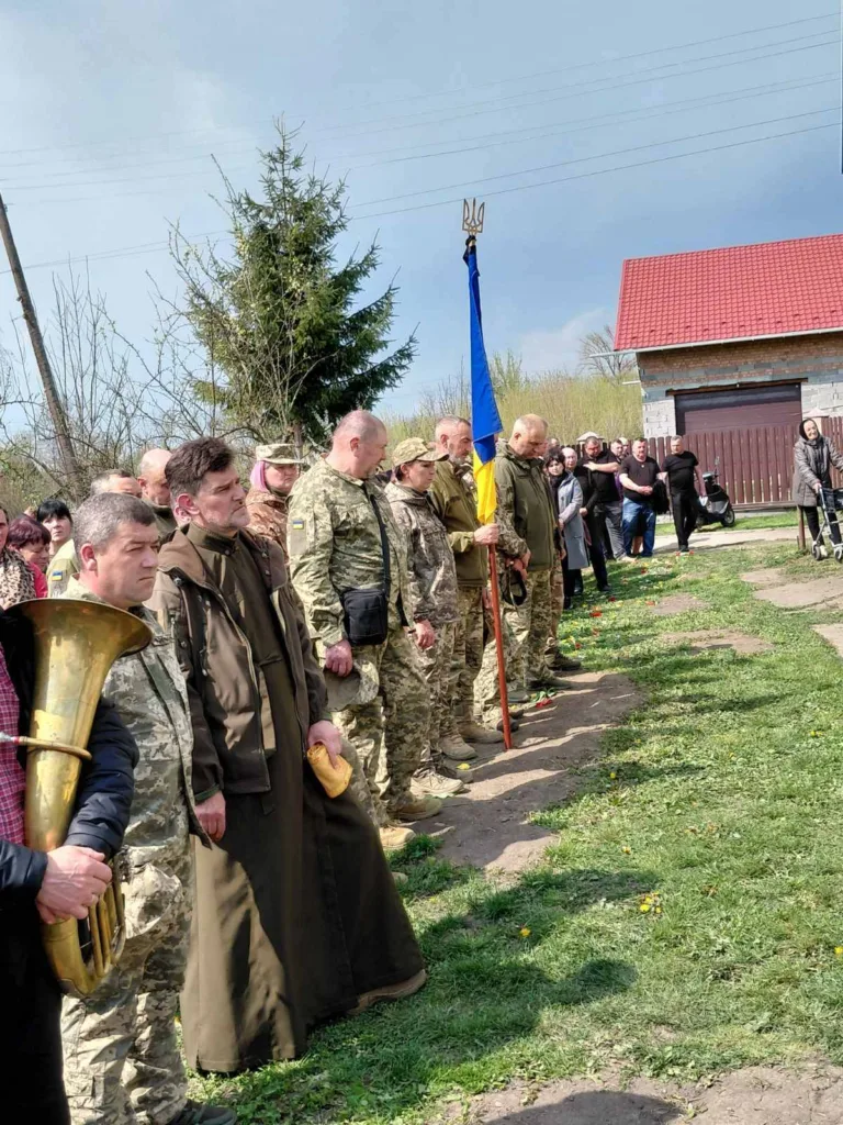 Військові та священник стоять з українським прапором