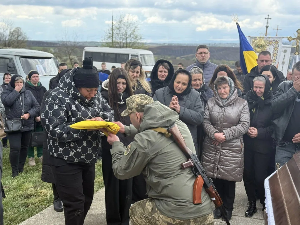 Військовий передає прапор скорботній родині на похороні