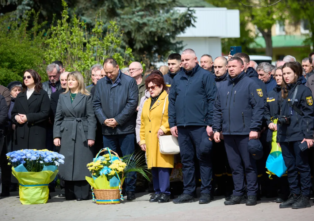 Люди стоять на урочистій церемонії з квітами