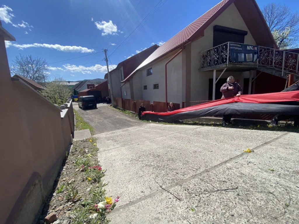 Люди розгортають великий червоно-чорний прапор біля будинку