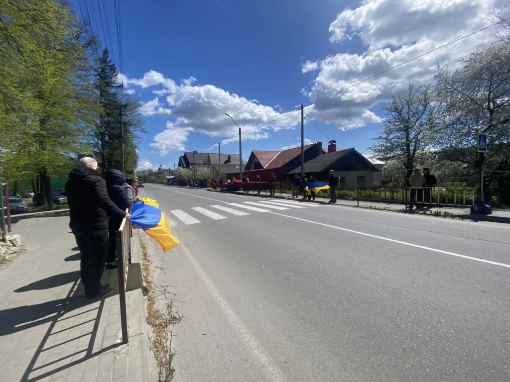 Люди з українськими прапорами стоять біля дороги