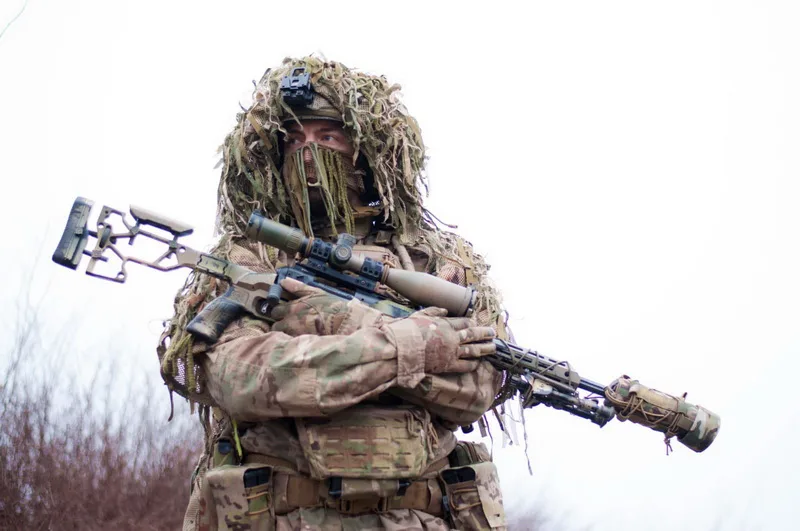 Снайпер у камуфляжі тримає гвинтівку на природі