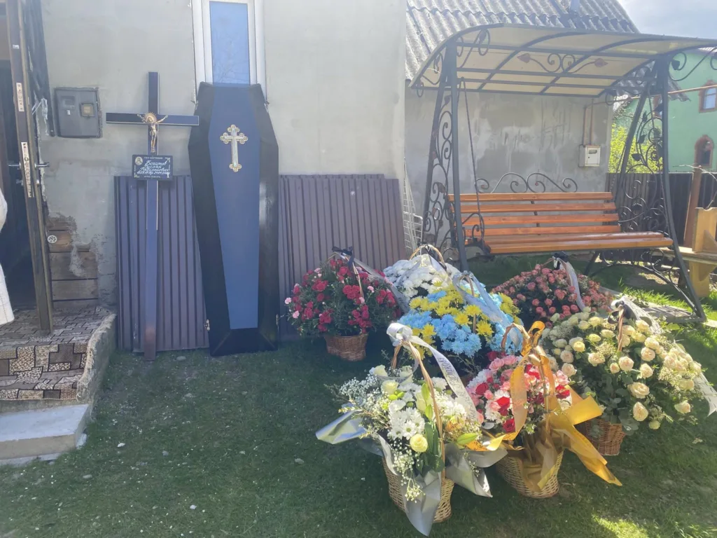 Труна, хрест і похоронні квіти біля будинку