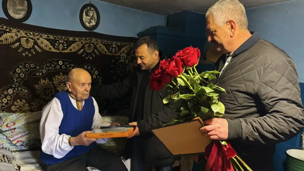 Чоловіки вітають літнього чоловіка з квітами та подарунками