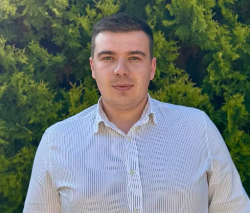 Чоловік у білій сорочці на фоні зелених кущів