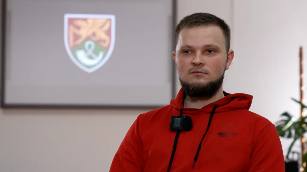 Чоловік у червоній худі сидить у приміщенні