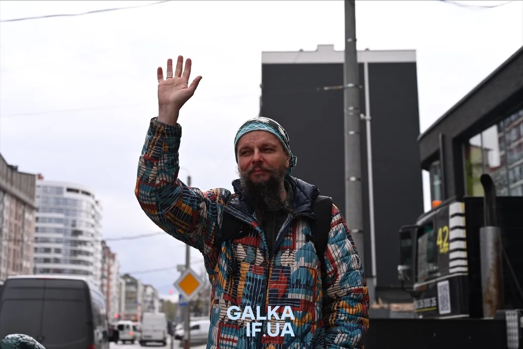 Чоловік у кольоровій куртці піднімає руку на вулиці