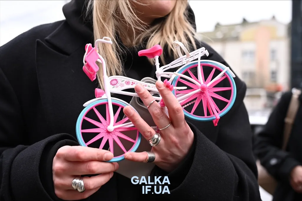Жінка тримає рожевий іграшковий велосипед