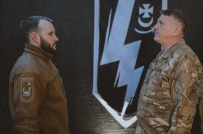 Двоє військових стоять перед прапором підрозділу