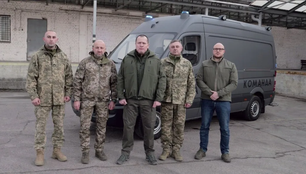 Військові стоять перед сірим мікроавтобусом