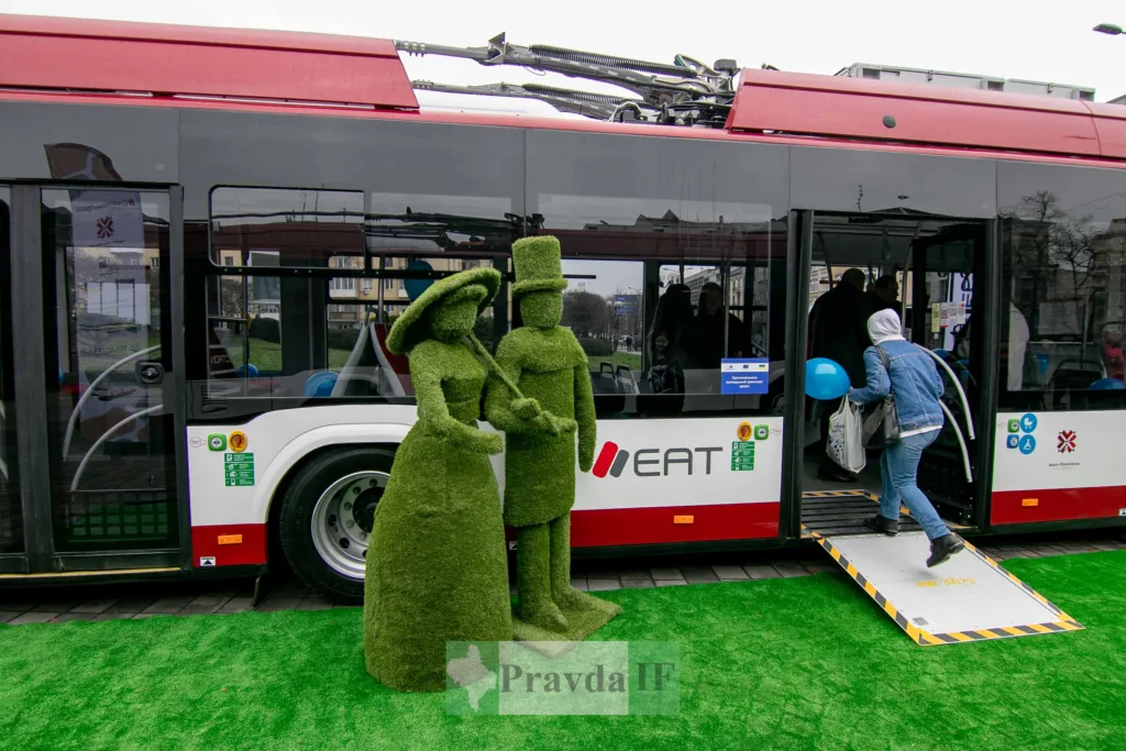 Люди сідають у сучасний тролейбус біля скульптур