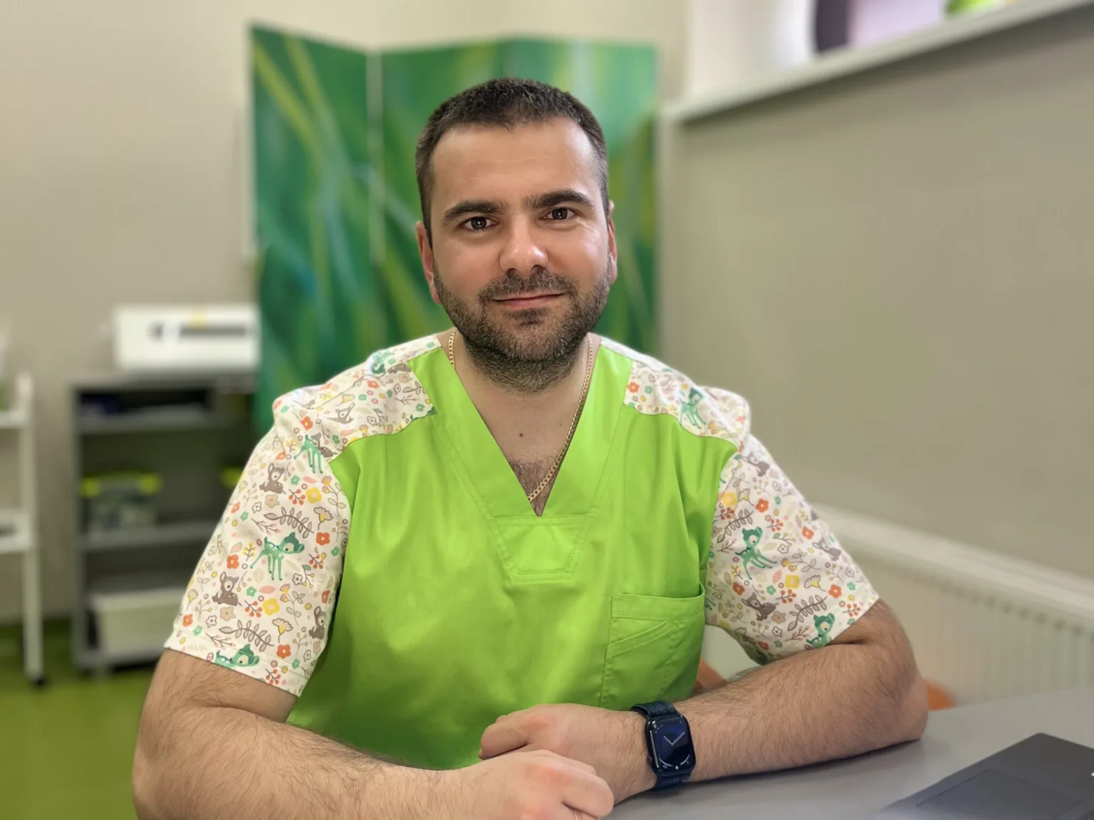 Усміхнений медик у зеленому халаті за столом